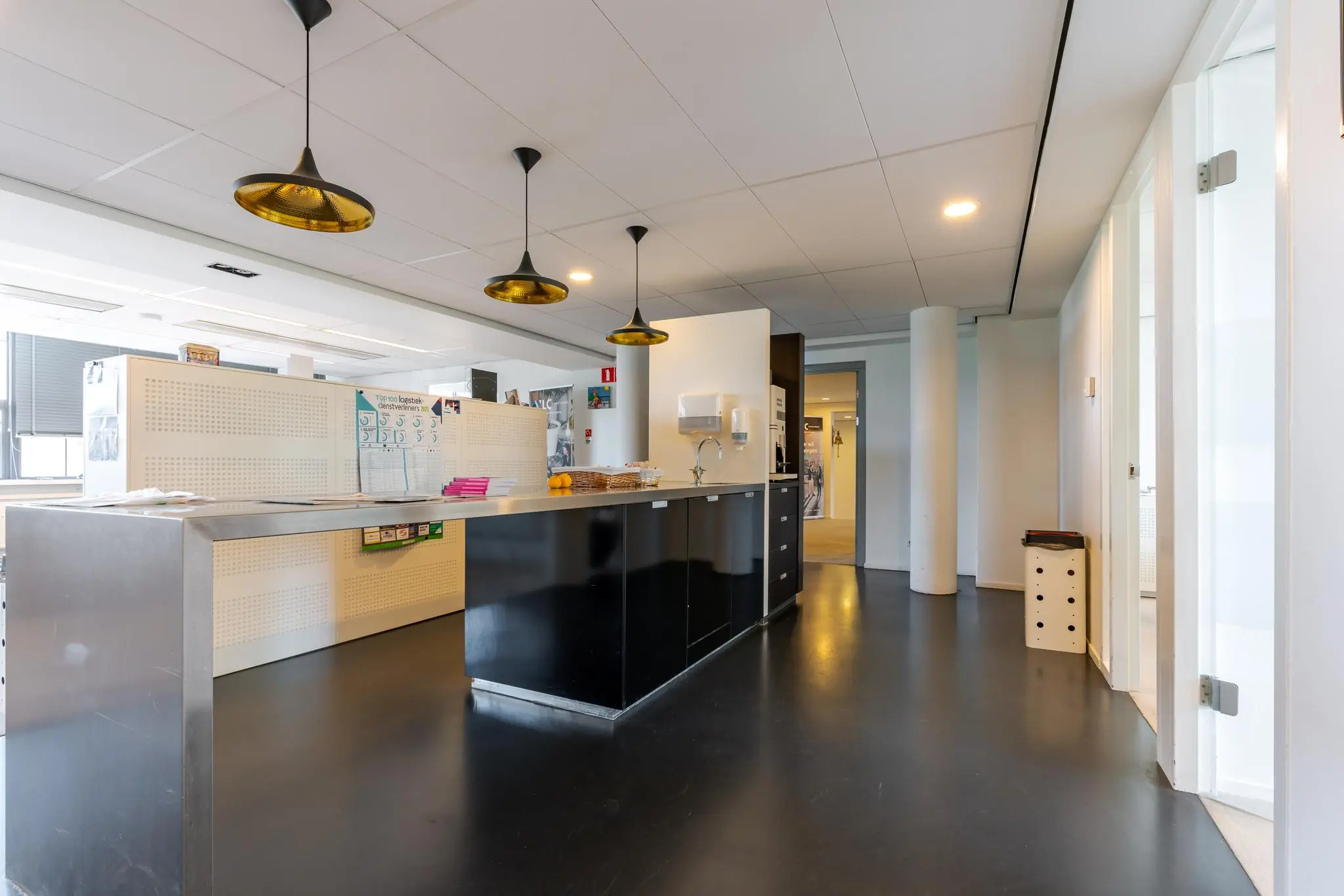 Moderne pantryruimte met zwarte keukenkasten, hanglampen en witte wanden in een kantoor aan de Van Alkemadelaan.